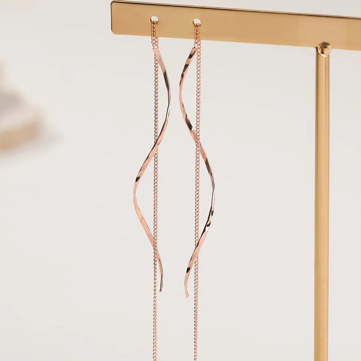 Emma & Rose Cape Town Phaedra™ gold long earrings with wavy design, showcasing elegant, flowing style in a close-up image.